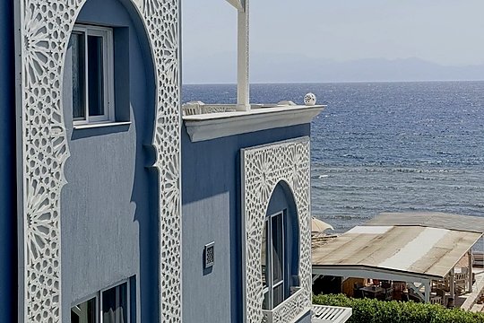 واجهة الفندق بلون البحر ونقوش مشربية بيضاء، وخلفها البحر الأحمر